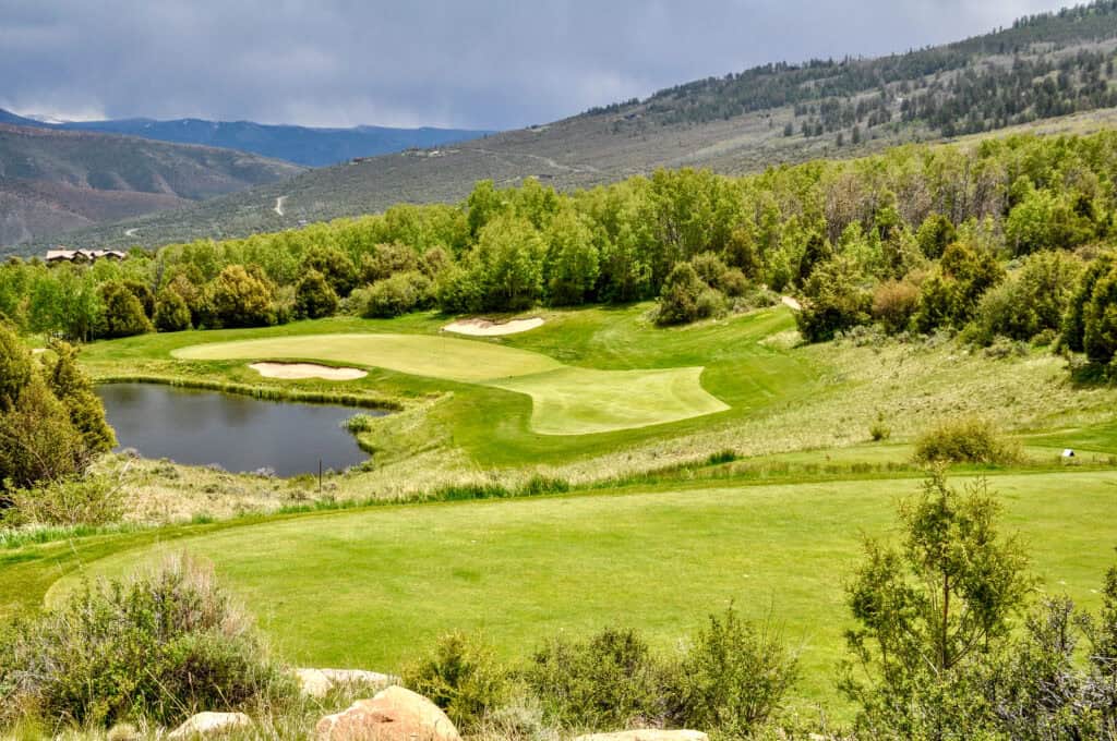 Scenic golf course with lush green fairways, water hazards, and surrounding mountains.