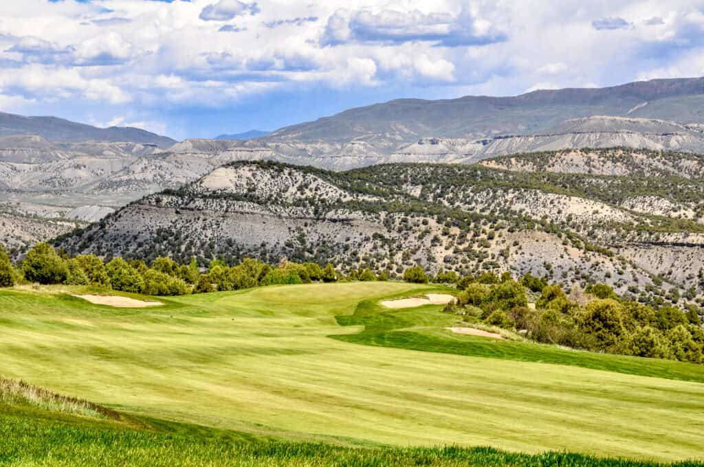Scenic view of a golf course with mountains in the background under a partly cloudy sky.