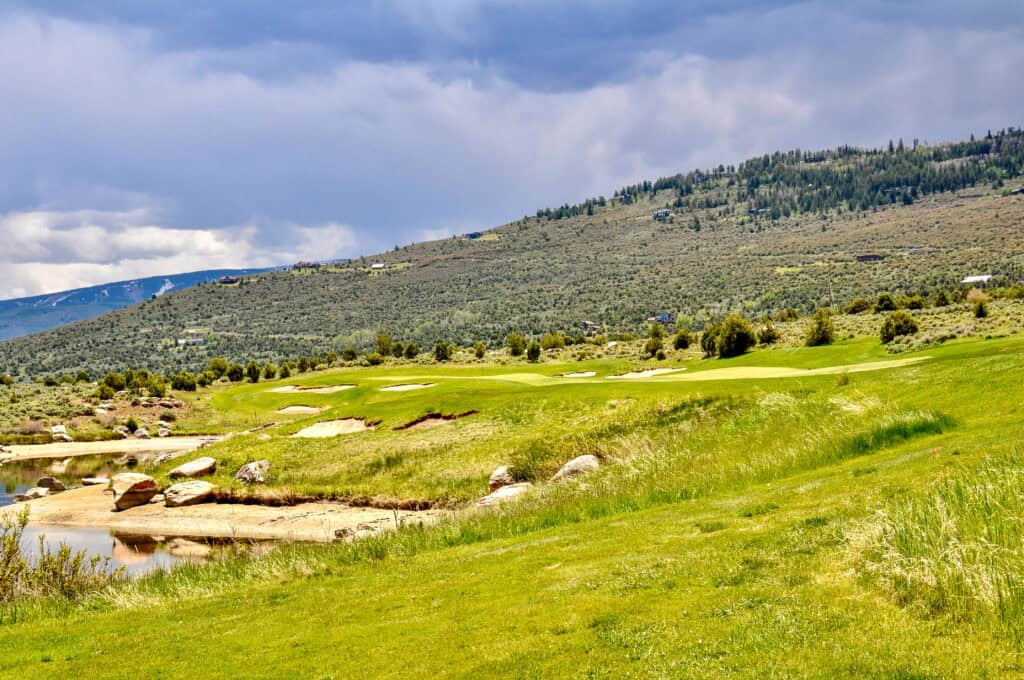 Scenic view of a golf course with mountains in the background and a cloudy sky.