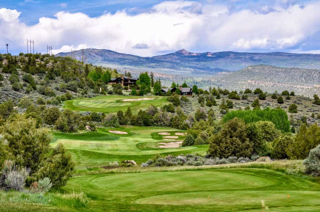 Scenic view of a golf course surrounded by lush greenery and rolling hills.