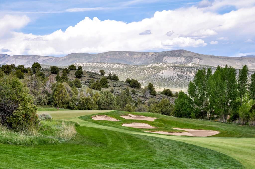 Scenic golf course with sand traps and mountain backdrop in bright daylight.