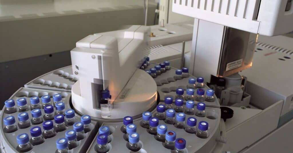 Automated laboratory machine handling multiple small vials with blue caps, used for amino acid analysis and supplement production at Amino Pharm.