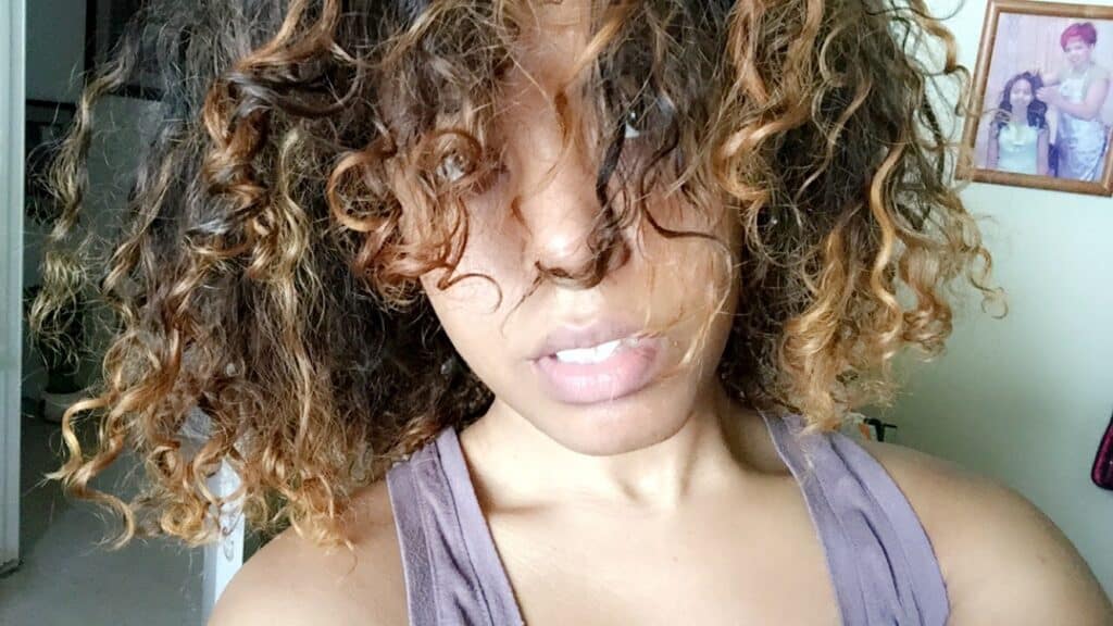 Natural curls with visible dye damage and dryness, covering face partially
