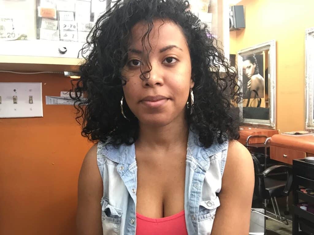 Woman with mid-length natural curls sitting in a salon, showing hair texture and growth after transition.