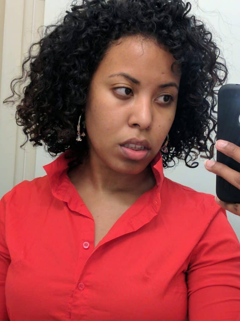 Side profile of a woman with defined natural curls in a red collared shirt, showing improved curl pattern and healthy hair texture