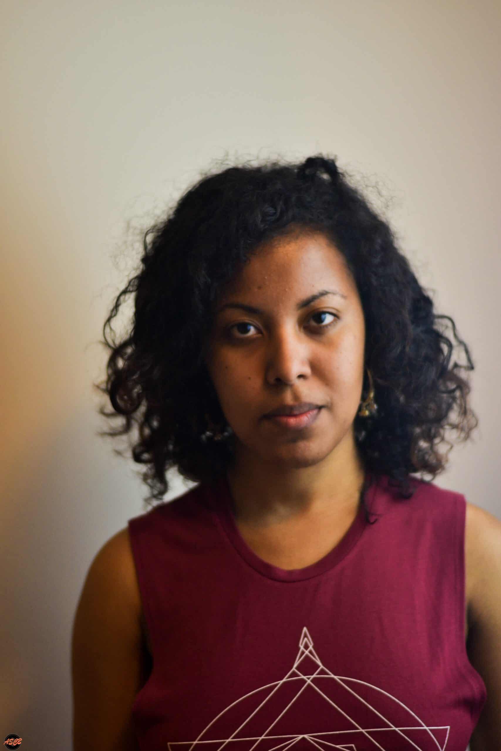Smiling woman with natural curly hair wearing a maroon tank top, showcasing healthy curls in natural lighting.