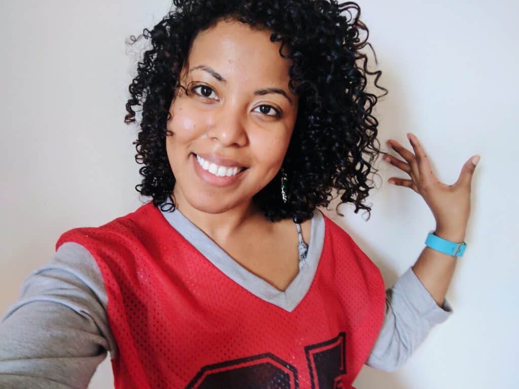 Smiling woman with curly hair wearing a red sports jersey, showing hair results after air-drying and styling