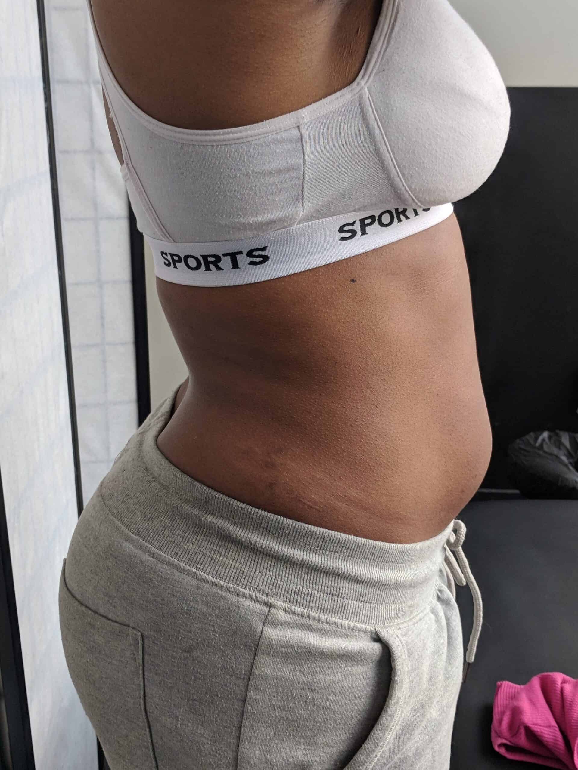 Close-up side profile of a woman wearing a sports bra and joggers, showing visible waistline definition and abdominal progress.