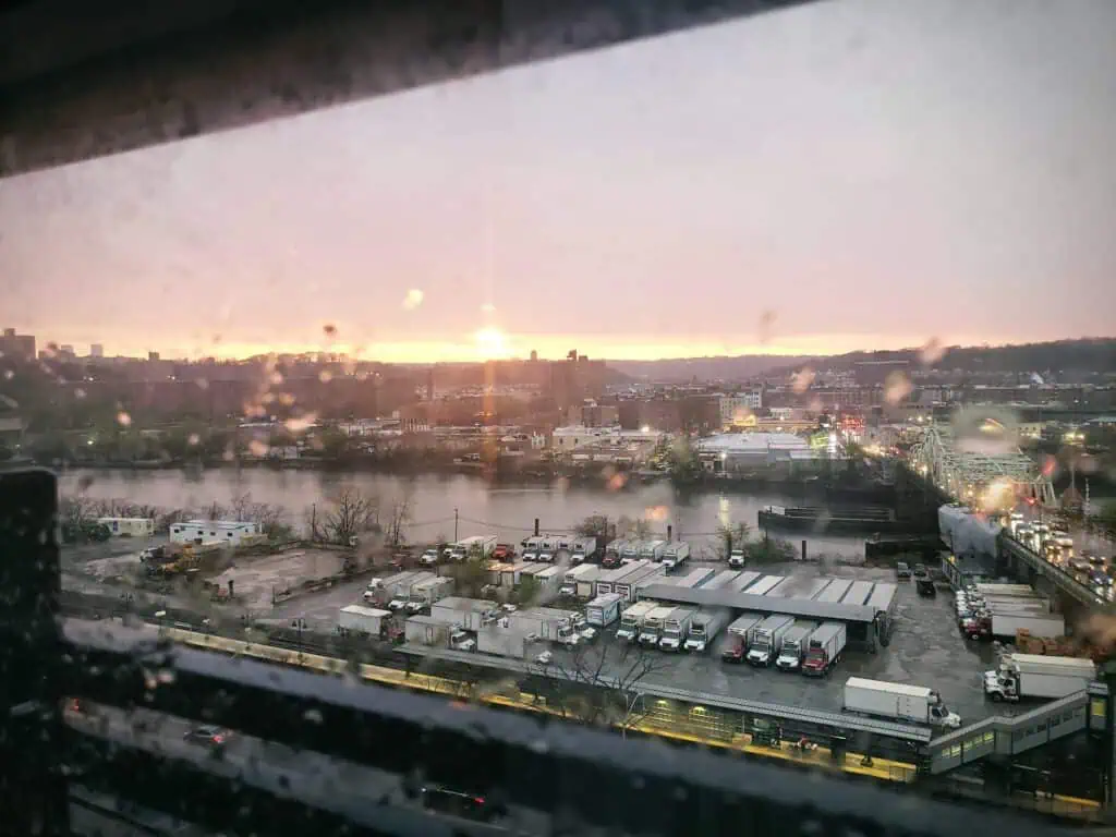 View from above overlooking Bronx rooftops and streets at dusk, with the city skyline glowing in the distance.