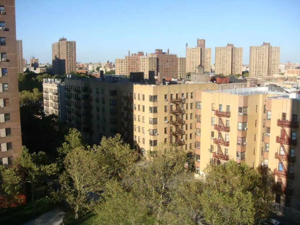 Aerial view of historic Bronx apartment buildings with classic fire escapes, set against a bright blue sky and tree-lined streets.