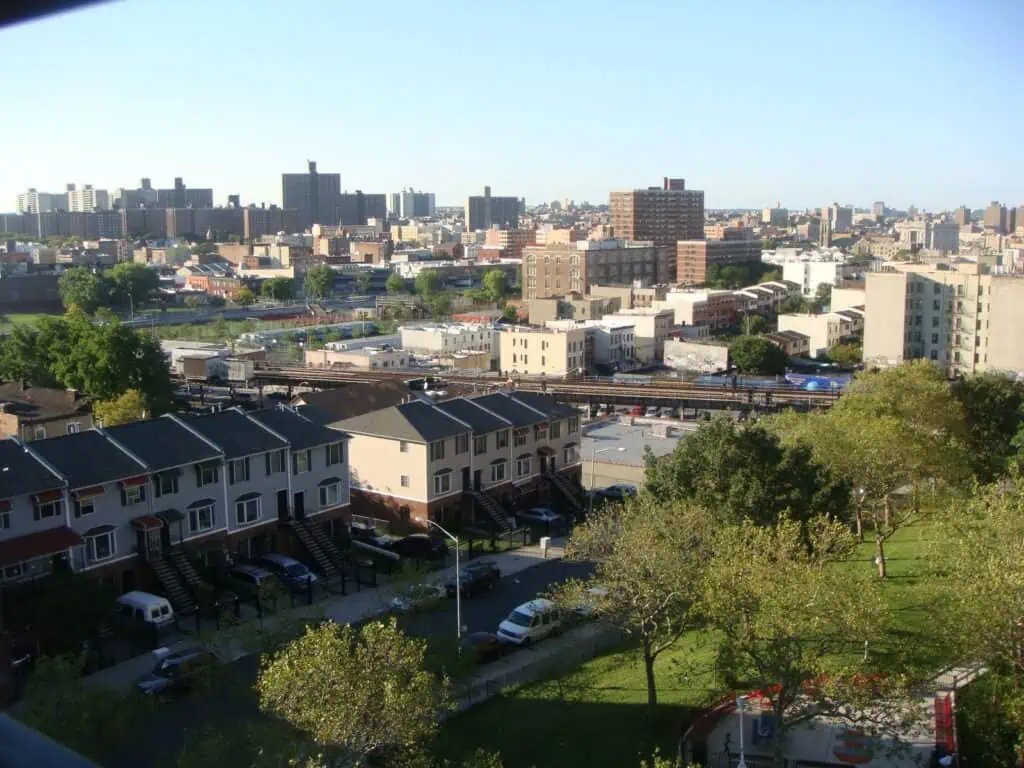 Elevated view of colorful townhomes and green space in the South Bronx, with high-rise buildings and train tracks in the distance on a clear day.