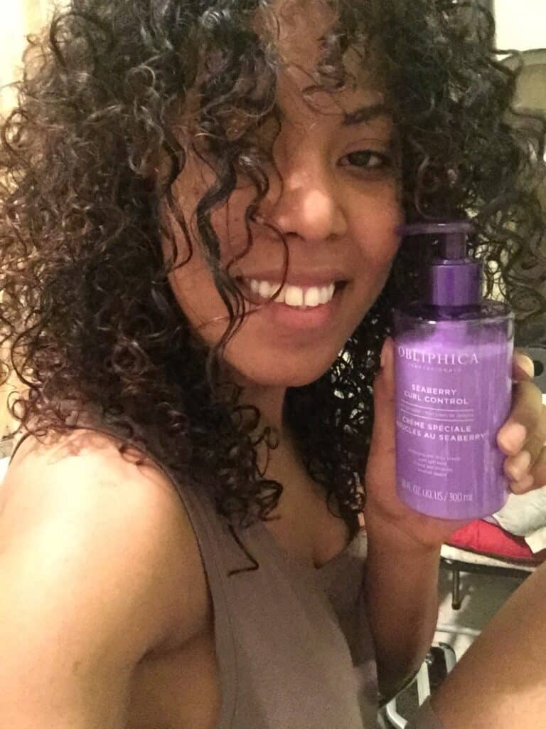 Close-up of a woman holding Obliphica Seaberry Curl Control cream, showing fresh curl results.