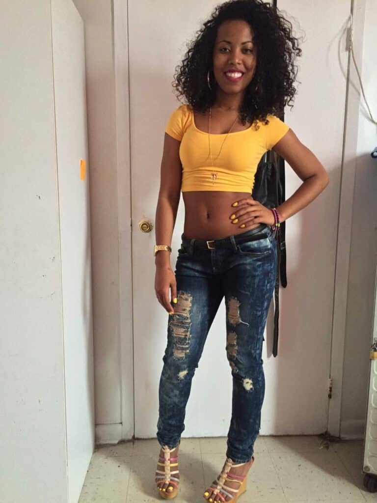 Woman in yellow crop top smiling confidently, showing off bouncy, defined curls.