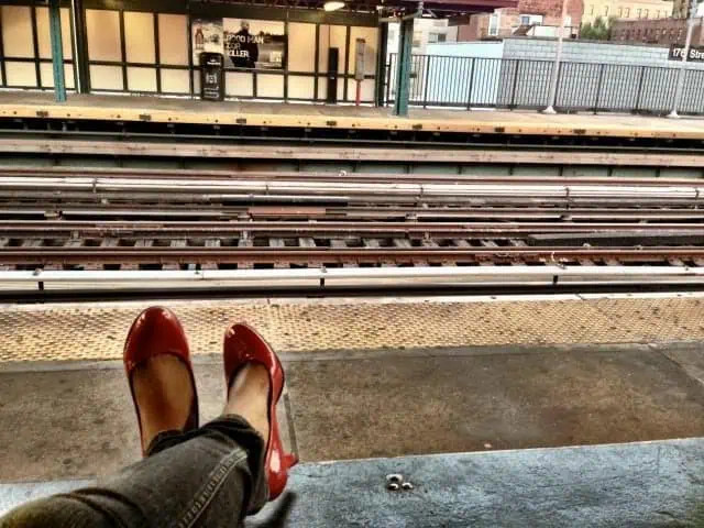 Person wearing red shoes sitting near elevated subway tracks in the Bronx, capturing a quiet moment at the station.