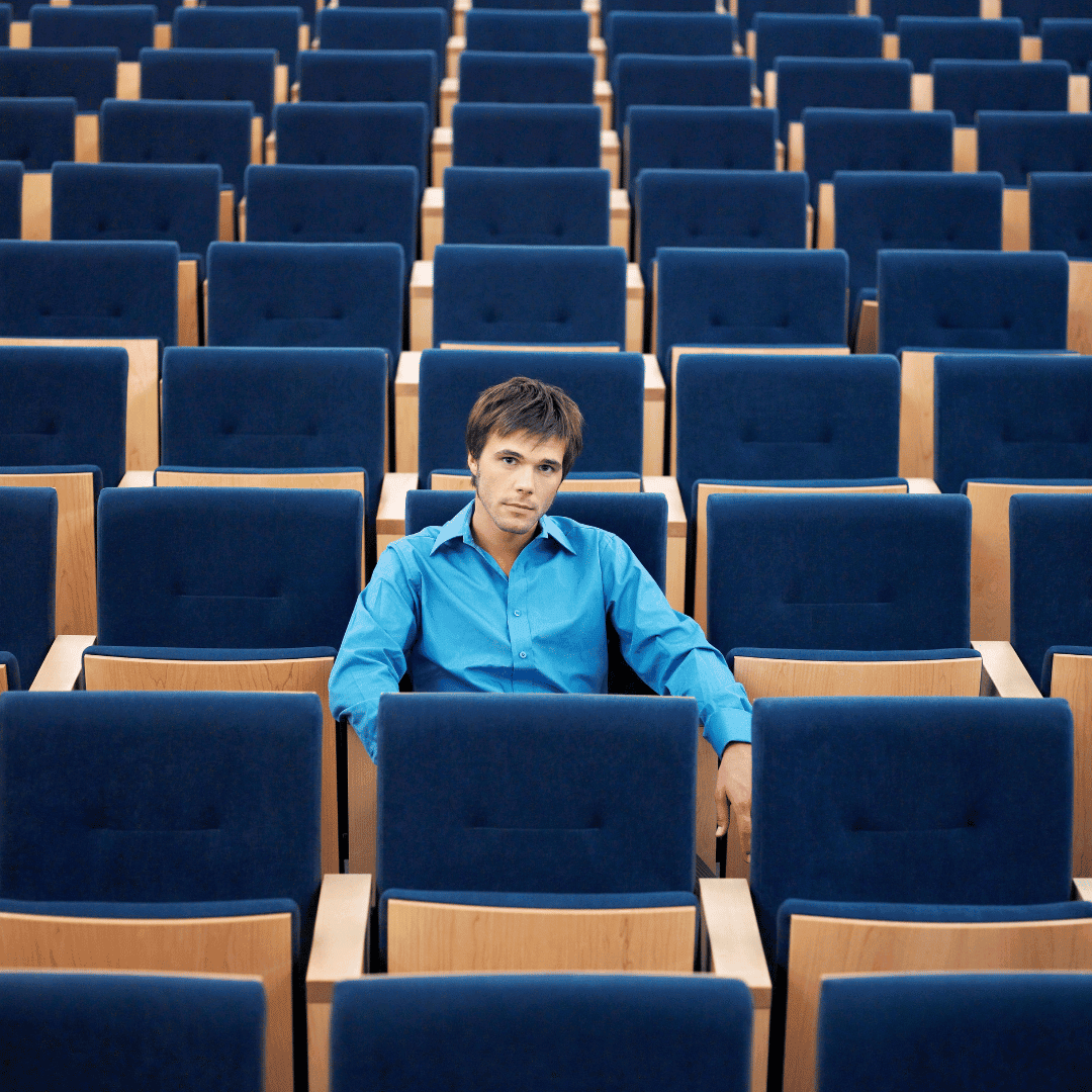 Individual seated in a large auditorium with many empty seats