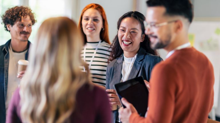 Happy diverse colleagues have fun at lunch break in office, smiling multiracial employees laugh and talk drinking coffee