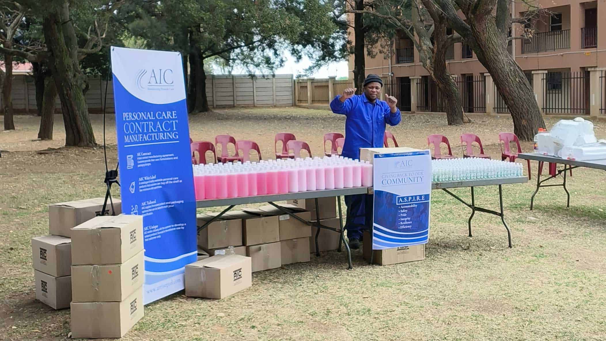 AIC community health initiative with hand sanitiser bottles at outdoor event in South Africa.