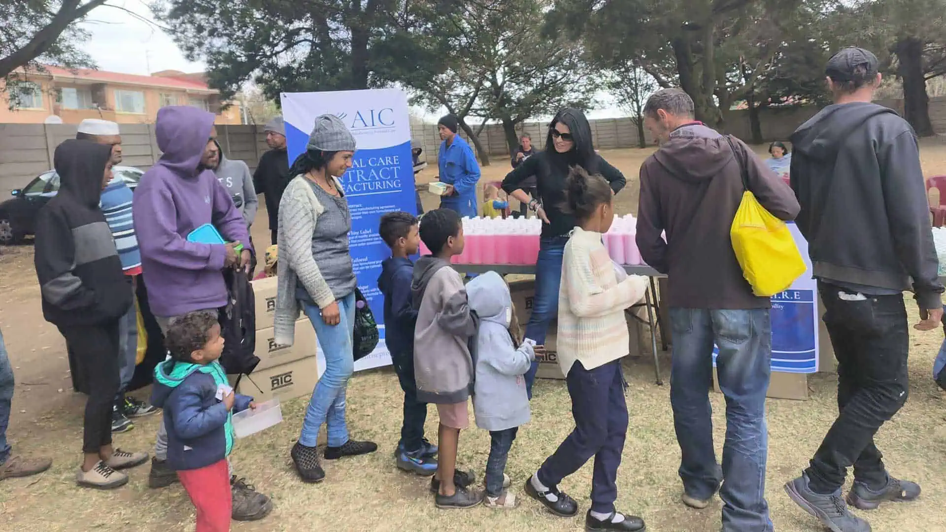Community health event with children and adults at AIC antiseptol booth in outdoor setting.