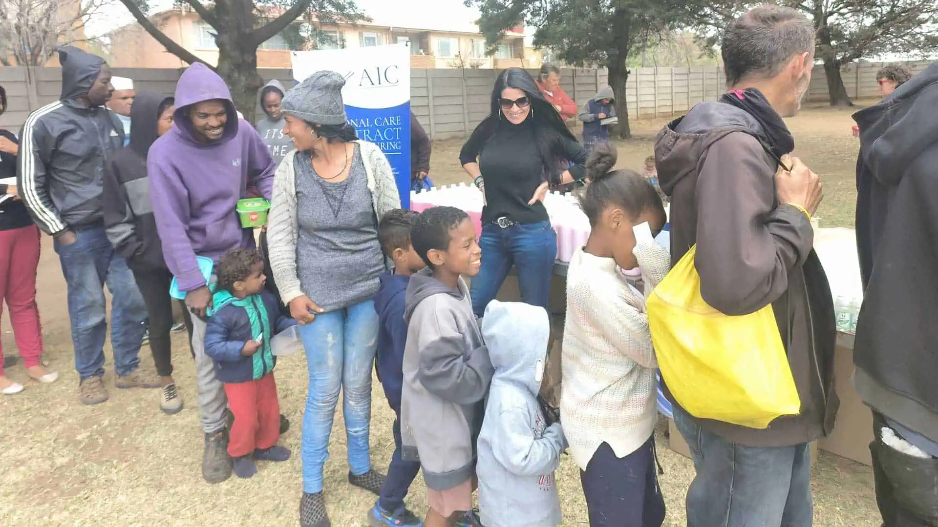 People queuing outdoors at AIC health clinic for medical services in a community setting.