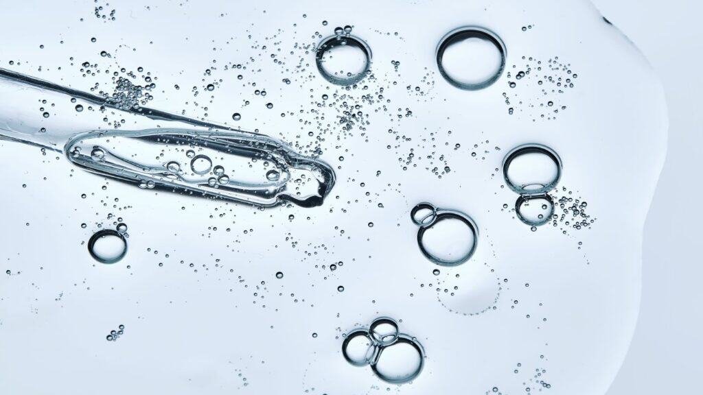 Close-up of a dropper releasing serum into water with bubbles.