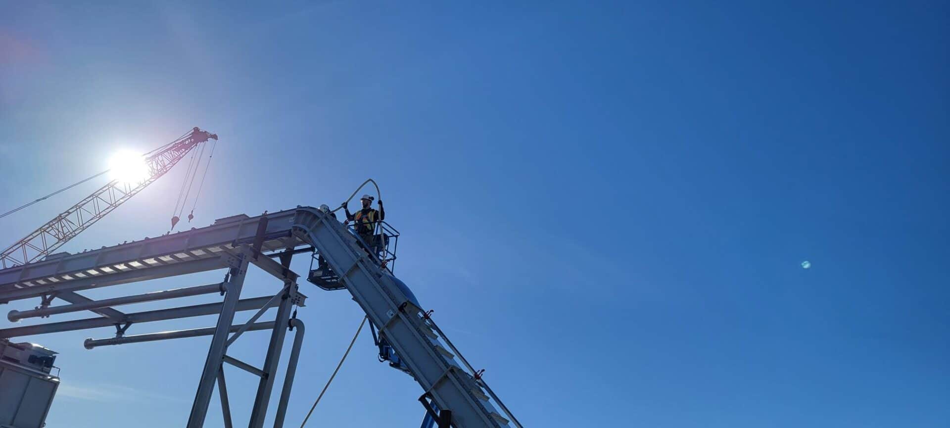 A man sits atop a structure against a blue sky