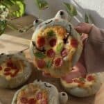 A playful green frog-shaped pizza made with spirulina dough, topped with gooey melted cheese and pepperoni slices arranged on its belly. A fun, cheesy treat perfect for kids and animal-shaped pizza lovers