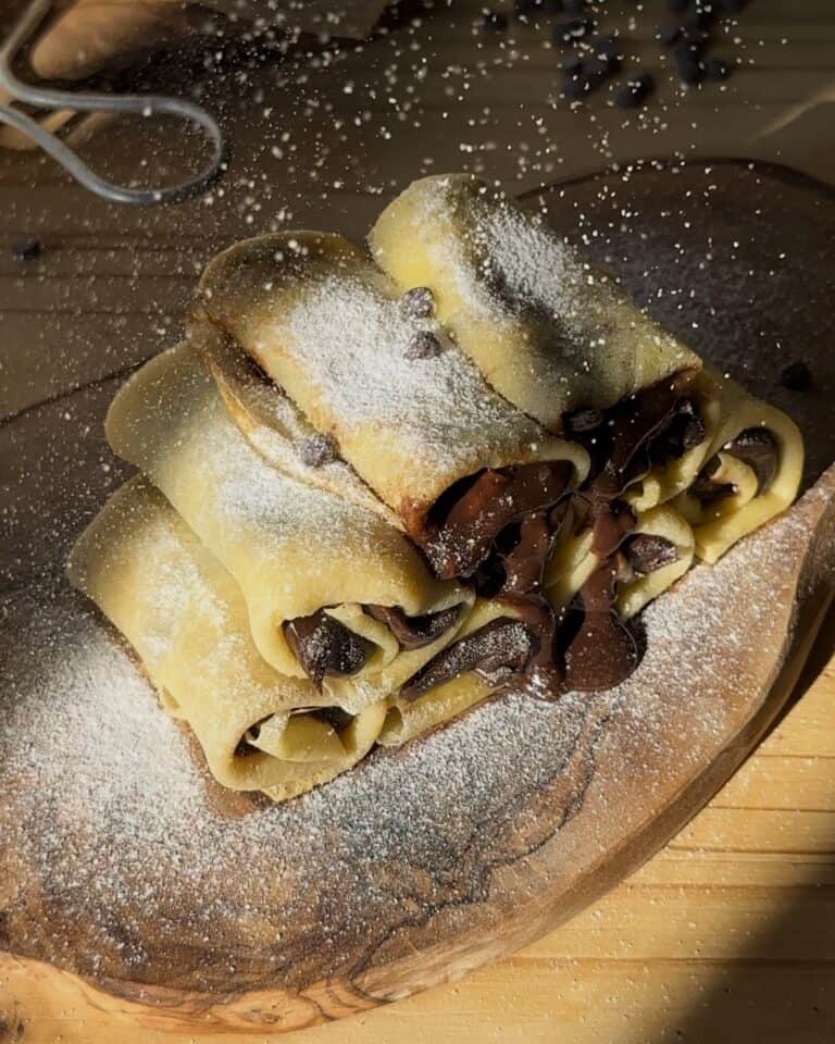 Adding a dusting of powdered sugar to the chocolate crepe rolls, enhancing their sweetness and ready to be enjoyed