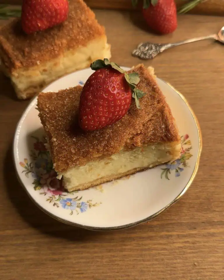 Churro cheesecake bars served with a fresh strawberry on a delicate flower plate