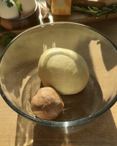 Jellycat croissant dough ready to proof, resting in a bowl covered with plastic film for a fluffy texture