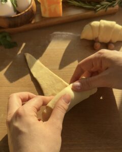 rolling the triangle-shaped Jellycat croissant dough with cheese before baking
