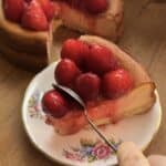 A single slice of creamy cheesecake on a plate with fresh strawberries and jam, as a spoon digs into the smooth filling, creating a tempting dessert moment.