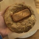 Image of a freshly baked Biscoff stuffed cookie held in hand, showcasing crispy golden edges and a gooey center with visible Biscoff spread and a Biscoff cookie in the middle, highlighting the delicious, indulgent texture.