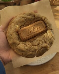 Image of a freshly baked Biscoff stuffed cookie held in hand, showcasing crispy golden edges and a gooey center with visible Biscoff spread and a Biscoff cookie in the middle, highlighting the delicious, indulgent texture.