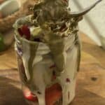 A fork digging into a jar of White Chocolate Dubai Strawberries, with a juicy strawberry on the fork. The top of the strawberry is covered with a mixture of crispy toasted kataifi and creamy pistachio, creating a delightful blend of textures and flavors.