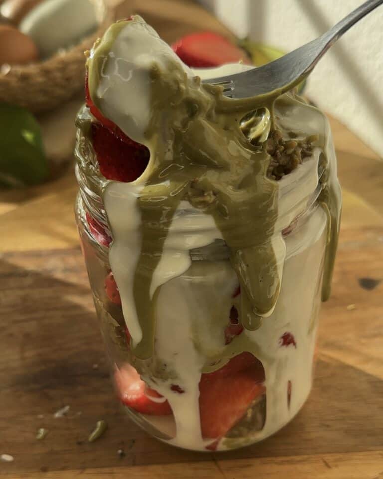 Close-up of a fork digging into a jar filled with White Chocolate Dubai Strawberries, showcasing the layers of creamy white chocolate, pistachio cream, and fresh strawberries. The indulgent layers are perfectly visible, making each bite a delightful mix of textures and flavors.