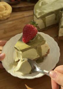 Slice of no bake pistachio cheesecake on a plate with visible crust, creamy filling, and pistachio topping, being scooped with a spoon to highlight texture