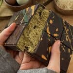 Homemade Dubai chocolate bar cut in half, showing layers of crunchy kataifi pastry and creamy pistachio filling, topped with rich chocolate.