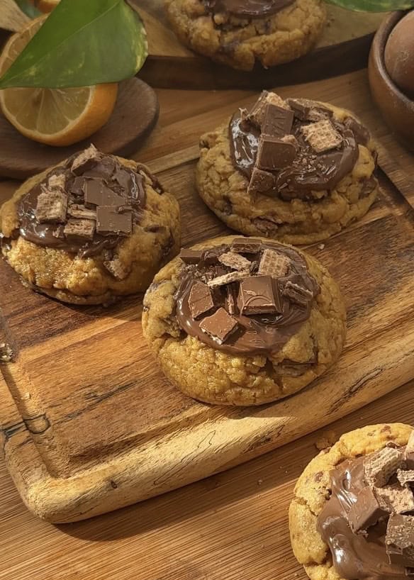 Homemade Copycat Crumbl KitKat cookies with a gooey texture, KitKat pieces inside, a rich chocolate spread on top, and extra KitKats for decoration.