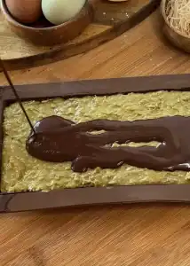 Pouring melted chocolate over a mixture of toasted kataifi, tahini, and pistachio cream in the chocolate mold for homemade Dubai chocolate bars.