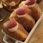 Fluffy strawberry cheesecake stuffed donuts with fresh strawberries on top, coated in sugar, showcasing their delicious filling.