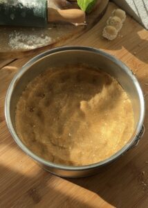 Pressing the cookie crust into a greased mold to create the perfect base for Happy Hippo No-Bake Cheesecake, ready to be filled with creamy hazelnut cheesecake and Kinder-filled layers.