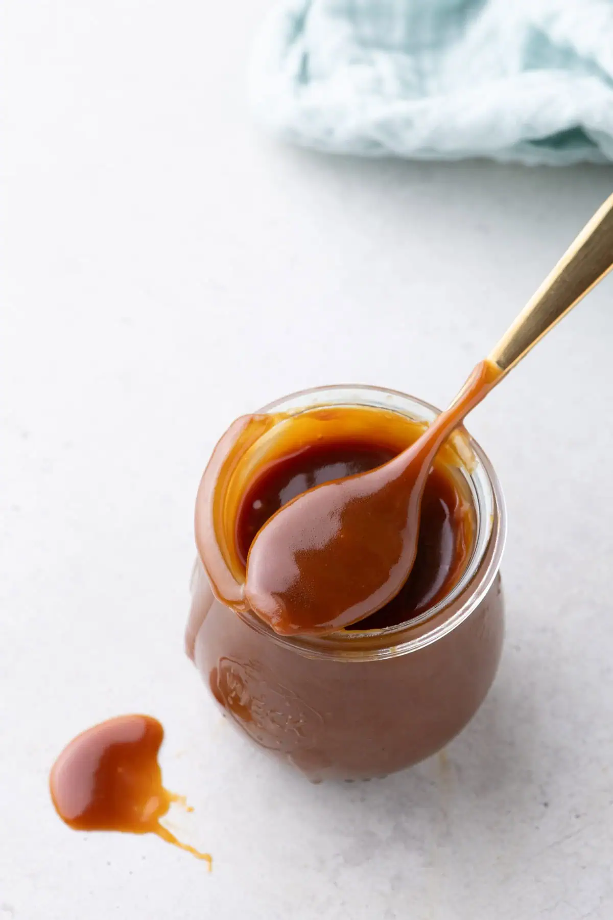 Overhead view of a jar of salted caramel sauce with a spoon and spilled caramel on white surface