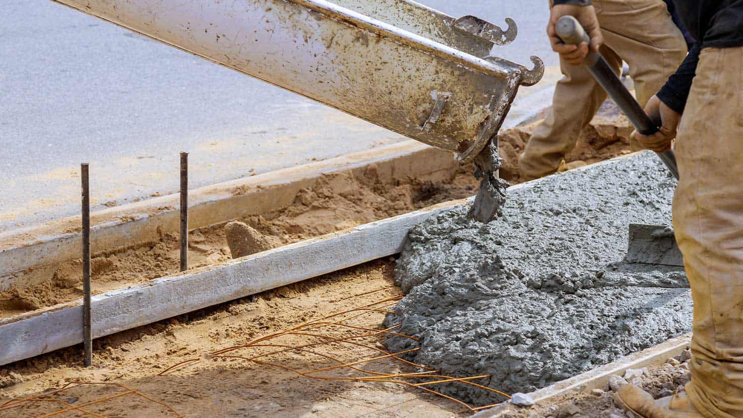 Workers pouring fresh concrete into a sidewalk pad