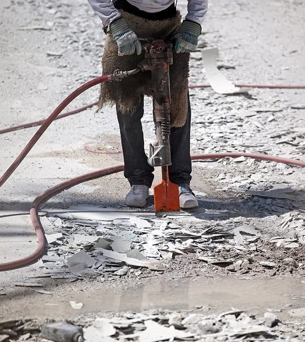 Worker destroying concrete sidewalk with jackhammer