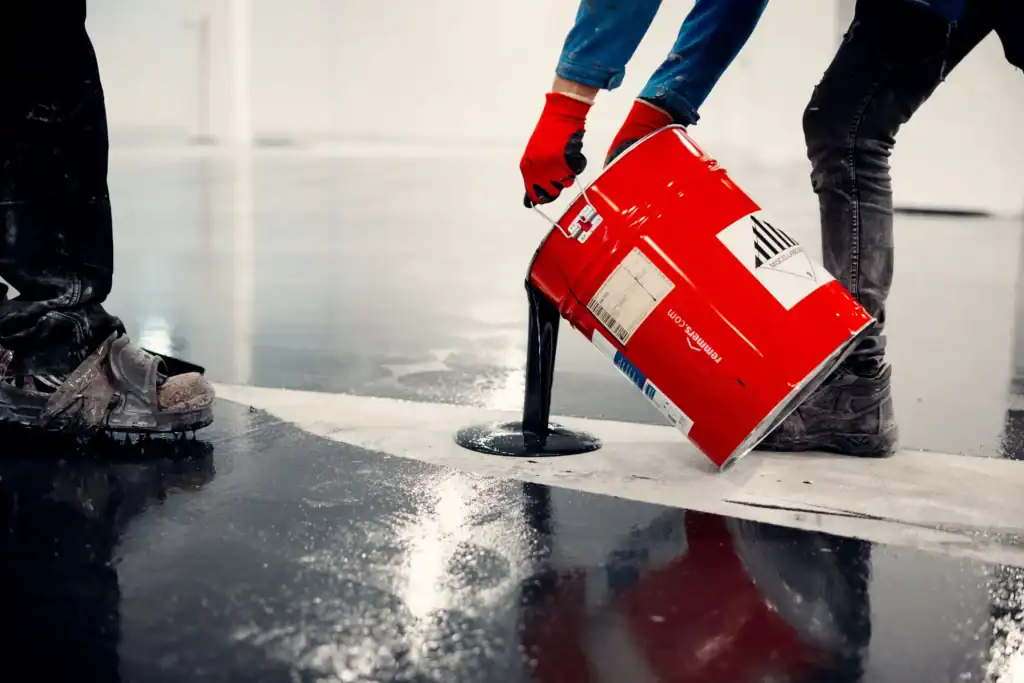 Worker sealing concrete floor with a caulking gun and sealant bucket, ensuring proper protection against cold weather damage.