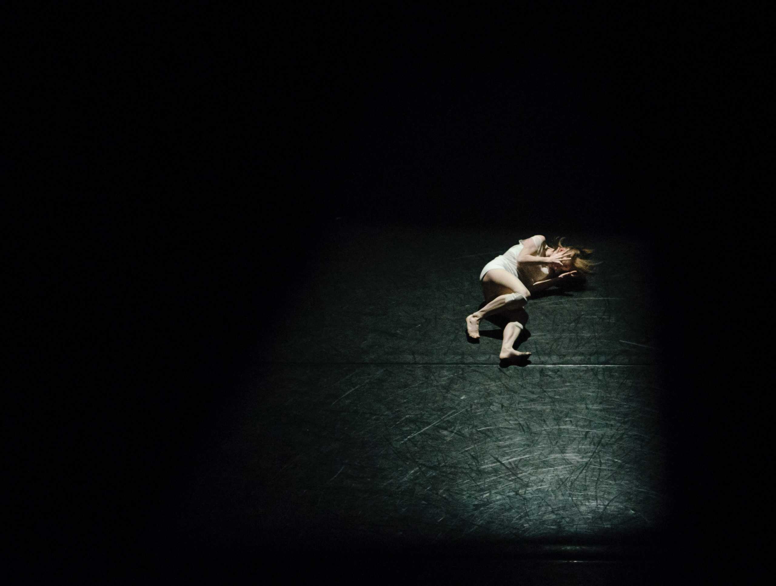 Photo of a female lying down on the ground with her hands to her head in discomfort.
