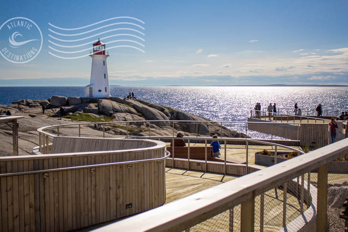 Lighthouse on rocky coast with ocean view, wooden boardwalk, and visitors enjoying scenic seaside in Atlantic Destinations, offering coastal excursions and travel experiences.