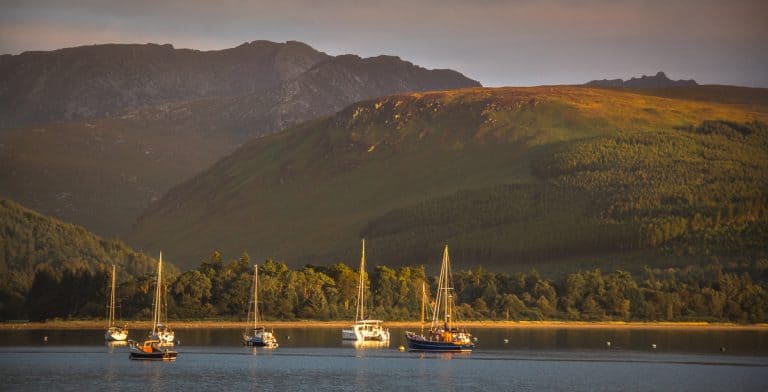 Serene harbor with sailboats against lush green mountains at sunset, showcasing Atlantic Destinations' scenic travel locations in the Atlantic region of the United States.