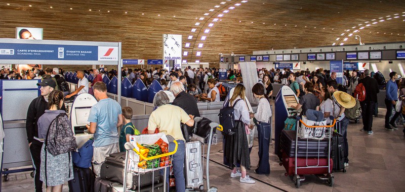 Passengers in line at an airport check-in counter with luggage for a travel destination.