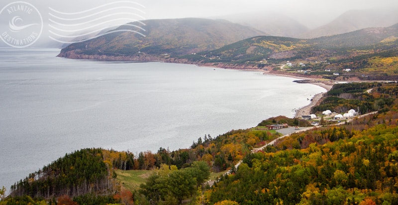Serene coastal landscape with lush autumn foliage, rolling hills, and a tranquil waterfront, showcasing scenic destinations in Atlantic Canada during fall.